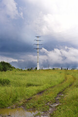 Obraz premium a country road in a field, a power line is on the horizon, contrasting heavy rain clouds in the sky, a summer day