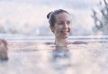 Happy woman enjoying hot thermal water in cold winter weather in snow. Relaxing bath in outdoor whirl pool in wellness spa. - 551051056