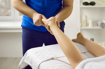 Male masseur in health clinic or massage parlor does hand massage of young woman's feet. Cropped...