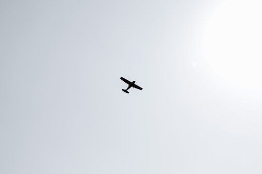 Black and white image of a single unidentifiable plane jet flying across the sky towards the shining sun