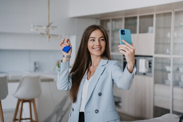 Pretty beautiful young woman in blue jacket shows keys of a new house to parents during video call...
