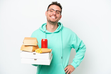 Young caucasian man holding fast food isolated on white background posing with arms at hip and smiling
