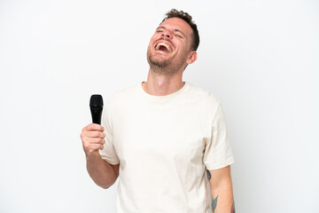 Young caucasian singer man picking up a microphone isolated on white background laughing