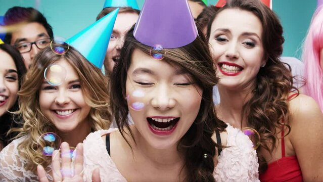 Bubbles, birthday party and happy friends, celebration and fun with dance, smile and energy in studio photobooth. Diversity group of people celebrate with soap bubbles, colorful hats and happiness