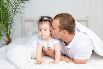 father and baby daughter on the bed under the blanket kissing and hugging. Happy family, Father's Day