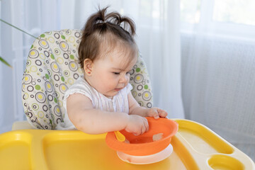 cute fat baby girl sitting in a high chair and eating food with her hands, baby food concept