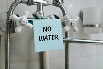 Text message No Water on self-adhesive sticker taped to bathroom faucet, close-up. Concept energy crisis, poverty, problem