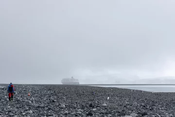 Fotobehang Hiker at the rocky and foggy shore in Antarctica © Freego/Wirestock Creators