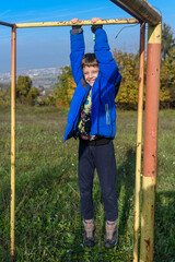 Kid doing pull ups on sports ground. Boy doing pull ups outdoors. The boy is doing pull-ups