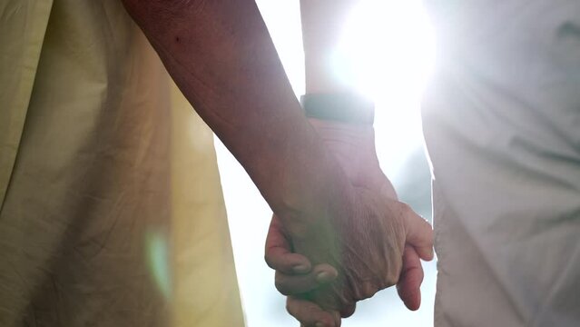 Close up of senior hands together with sunlight flare in the background. Beautiful romantic moment between two older married couple outdoors