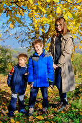 A sister with her younger brothers stands next to an autumn yellow tree
