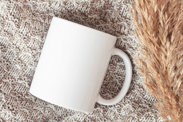 Mockup of white mug on knitted plaid with dried flowers, in neutral beige color. Blank coffee cup...