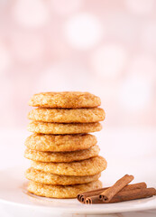 Stack of homemade snickerdoodle cookies with cinnamon sticks on a pink bokeh effect background with copy space