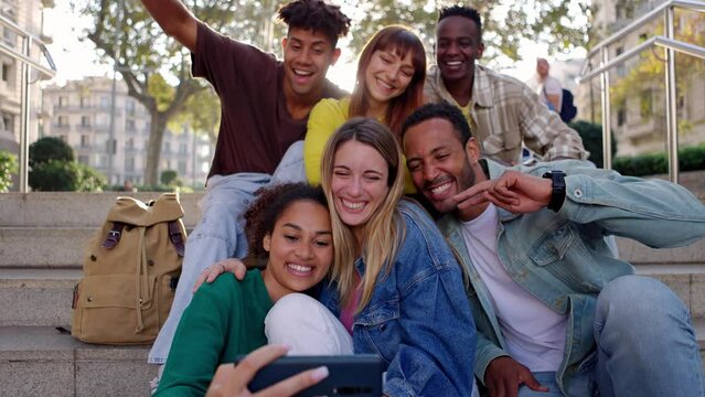 Happy young group of diverse people having fun taking selfie portrait while sitting together outdoors during travel holidays. Multiracial friendship and vacation concept