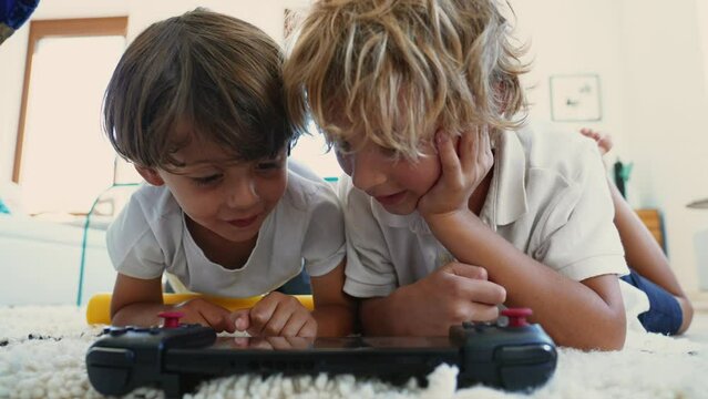 Excited brothers looking at tablet screen lying down together. Portrait of kids watching media online smiling