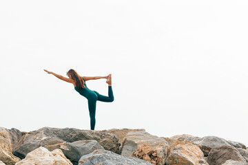 Woman practicing yoga, stretching in Natarajasana exercise, Lord of the Dance pose. Female in green sportswear working out, training outdoors, full length. King dancer. Healthy lifestyle concept.
