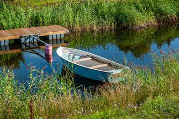 Naklejka na ściany i meble A small fishing boat lies in the wonderful and idyllic backwater. Boat at the pier on a sunny summer day.