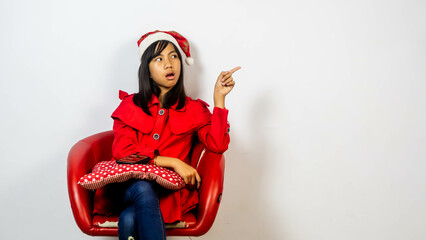 little girl in santa suit sitting on a red chair isolated on white background