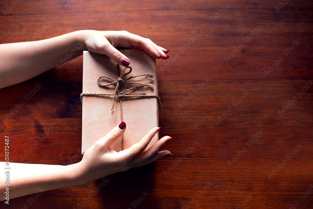 Canvas Prints Female hands hold gift box on dark brown wooden background	