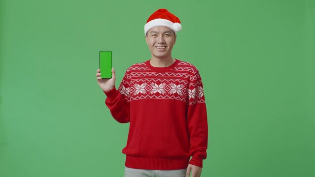 Asian Man In Santa Suit With A Smile Using A Laptop While Standing On Green Screen In The Studio
