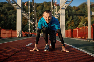 Adult speed runner in starting position ready for running on sports track