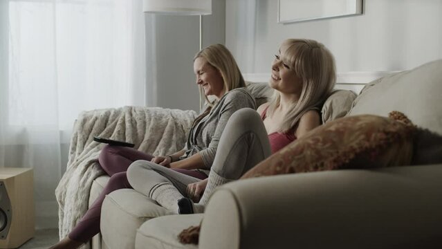 Tilt up to women sitting on sofa watching television and laughing / Cedar Hills, Utah, United States