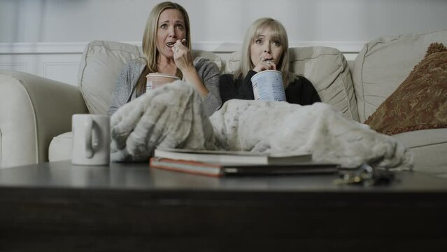 Tilt up to sad women sitting on sofa eating ice cream and watching television / Cedar Hills, Utah, United States