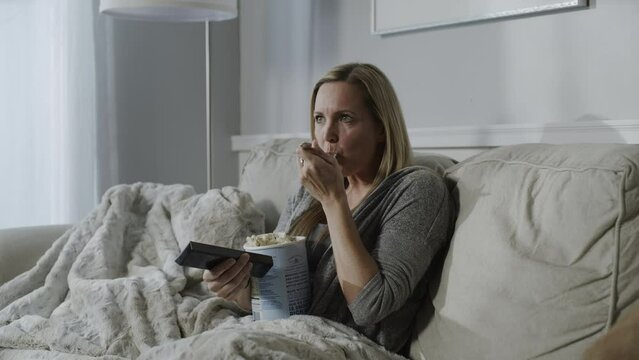 Woman sitting on sofa eating ice cream and watching television / Cedar Hills, Utah, United States