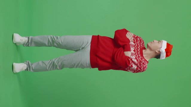 Full Body Of Offended Asian Man In Santa Suit Crossing His Arms And Looking Around While Standing On Green Screen In The Studio
