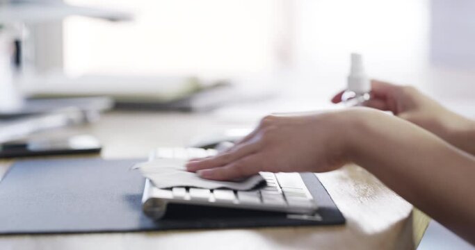 Hands, sanitizer and cleaning dust on keyboard at office desk for bacteria, virus or hygiene for health and safety. Worker spraying or wipes messy or dirty computer equipment for a healthy workspace
