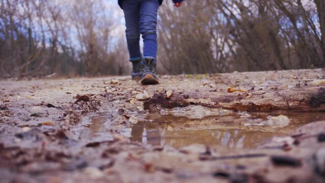 boy walks over a puddle on a path in the woods