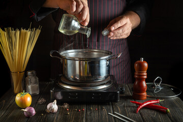 Cooking soup by the hands of the chef in the kitchen of the restaurant. The cook adds vegetable oil to the pan