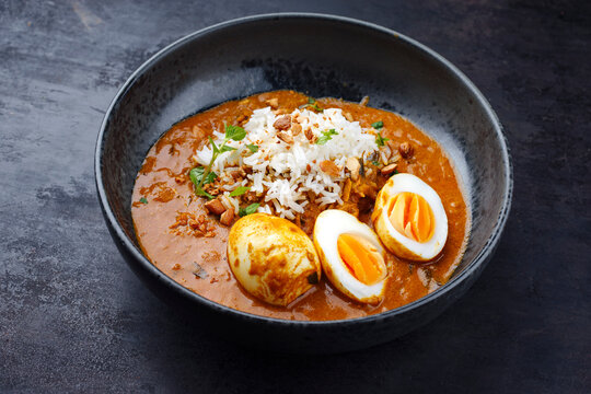 Traditional spicy Indian anda masala curry Rogan Josh with cooked eggs and basmati rice served as close-up in a Nordic design bowl with copy space