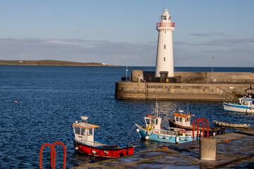 White lighthouse and colorful traditional fishing boats at the harbor. Donaghadee harbour, Northern Ireland, UK