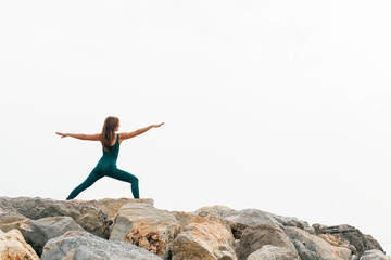 Peaceful focused woman standing in Warrior Two exercise yoga, Virabhadrasana 2 pose, wearing green sportswear. Working out, full length. Outdoor training. No stress and health care concept...