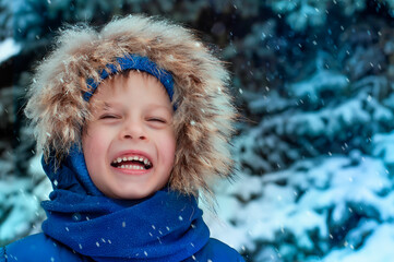 A child dressed in winter clothes smiles against the background of a snow-covered Christmas tree, it is snowing. High quality photo