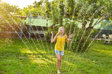 Happy kid girl playing with garden sprinkler run and jump, summer