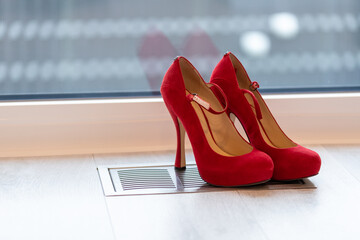Red high heel pumps in front of a window and on a light floor