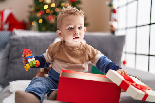 Adorable toddler unpacking christmas gift sitting on sofa at home