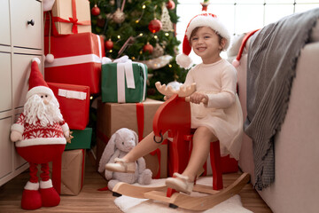Adorable girl sitting on rocking reindeer by christmas tree at home