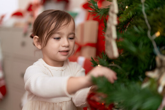Adorable girl decorating christmas tree standing at home