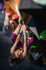 A young, slender, athletic climber in a sports field climbs a boulder at a festival in a climbing center. A vertical frame.
