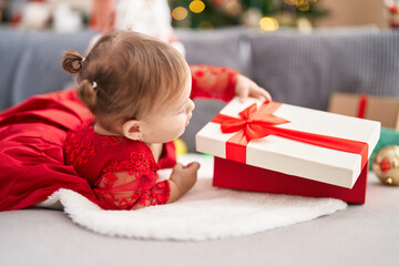 Fototapeta na wymiar Adorable hispanic girl unpacking gift lying on sofa by christmas tree at home