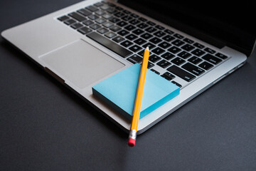 Open laptop in modern workplace with office supplies, mockup sticky note, a long yellow pencil