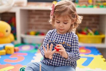 Adorable hispanic girl playing with hoops game sitting on floor at kindergarten