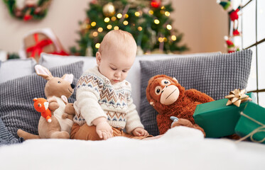 Adorable caucasian baby sitting on sofa by christmas tree with relaxed expression at home