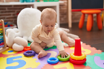 Adorable caucasian baby playing with hoops toy sitting on floor at kindergarten