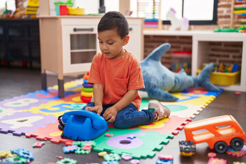 Adorable hispanic toddler sitting on floor playing with telephone toy at kindergarten
