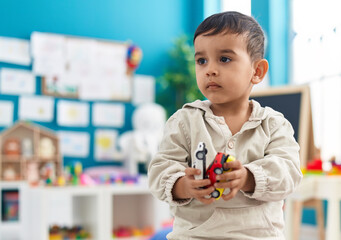 Adorable hispanic toddler holding car toy standing at kindergarten