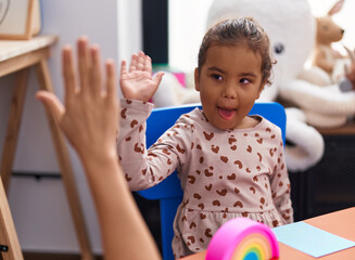 Adorable hispanic girl high five sitting on table at kindergarten